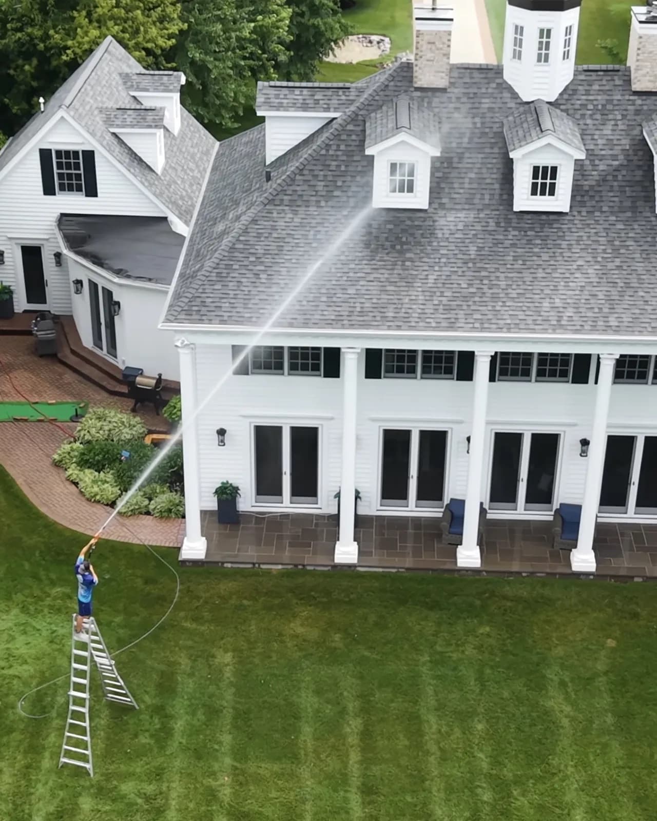 Aerial view of a Simmons crew member soft washing a white colonial home